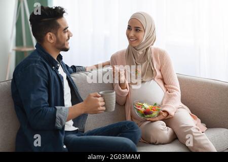 Schwanger Muslimische Dame In Hijab Essen Gemüsesalat Während Ehemann Kaffee Trinken Stockfoto