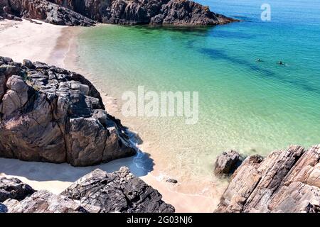 CLACHTOLL BEACH LOCHINVER SUTHERLAND SCOTLAND EIN KLEINER COVE SANDSTRAND FELSEN ZWEI SCHWIMMER UND KLARE GRÜNE WASSER IM FRÜHSOMMER Stockfoto