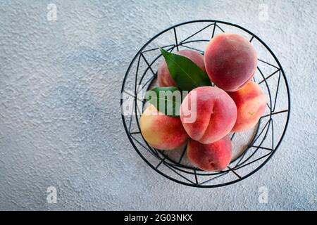 Frische Pfirsiche. Pfirsiche in Metallkorb auf hellem Beton Hintergrund. Flach liegend, Draufsicht, Kopierbereich Stockfoto