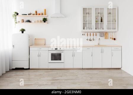 Neue Wohnung, moderne Renovierung. Weiße Küchenmöbel mit Utensilien, Regale mit Geschirr und Pflanzen in Töpfen Stockfoto