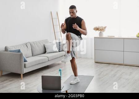 Schwarzer Mann Tut Stehende Knie Erhöhen Übung Bei Laptop Indoor Stockfoto