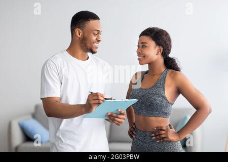 Junge schwarze Paar diskutieren Trainingsplan, zusammen zu Hause im Fitnessstudio stehen Stockfoto