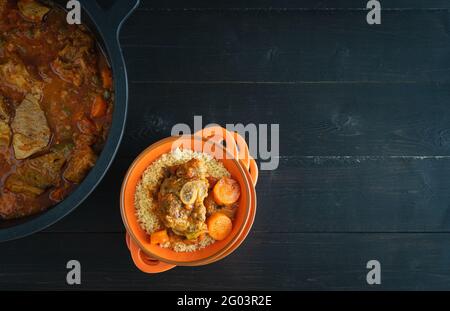 Schale mit Lamm mit Gemüse und Couscous auf schwarzem Holzgrund. Ramadan-Konzept. Speicherplatz kopieren. Draufsicht. Stockfoto