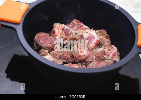 Lammfleisch, das in einer schwarzen Kasserolle gekocht werden kann. Kochkonzept. Stockfoto