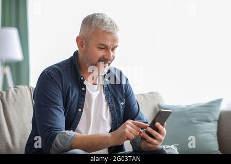 Lächelnder älterer Mann mit Smartphone zu Hause Stockfoto