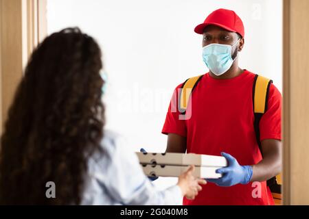 Schwarzer Lieferer in medizinischer Maske mit Pizzaboxen Stockfoto