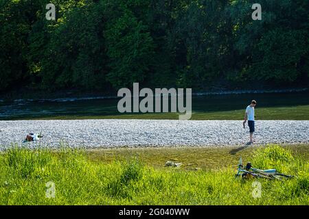 Ein Mann am Kiesstrand der Isar in München. Er steht mit seinen Füßen auf den Kieselsteinen und sieht einen türkisfarbenen Kreis im Wasser. Stockfoto