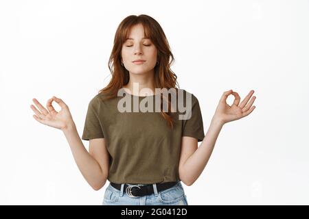 Behaltet die Ruhe und meditiert. Friedliche und entspannte junge Frau praktiziert Yoga, entspannt atmen mit geschlossenen Augen, Hände seitlich im Zen haltend, stehend Stockfoto