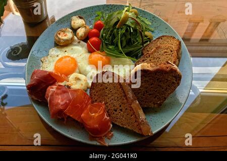 Frühstück mit Rührei mit Schinken, Gemüse und gerösteten Scheiben Schwarzbrot auf einem blauen Teller. Stockfoto