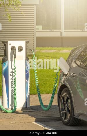 Nahaufnahme der Stromversorgung, die an ein graues Elektroauto angeschlossen ist, das aufgeladen wird. Stromversorgung für das Laden von Elektroautos Stockfoto