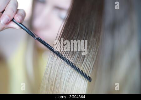 Eine Haarsträhne in Nahaufnahme. Der Vorgang des Kämmens mit einem dünnen schwarzen Kamm. Stockfoto