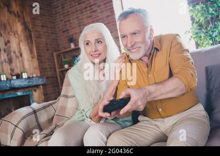 Foto von glücklichen schönen charmanten grauhaarigen Paar sitzen Sofa Smile Play Spielunterstützung drinnen in der Wohnung Stockfoto