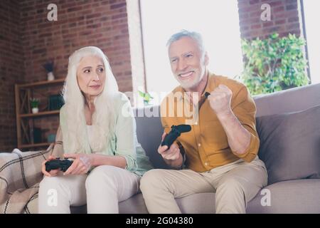 Foto eines Rentners mit grauem Haar, das auf dem Sofa spielt Spiel Joystick Mann gewinnen drinnen im Haus Stockfoto