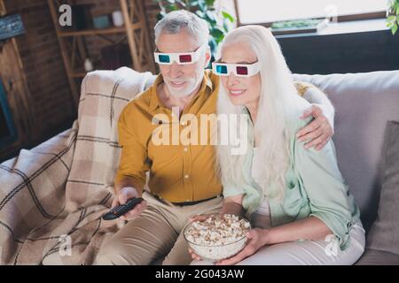 Porträt eines attraktiven älteren fröhlichen Paares, das auf dem Sofa sitzt und sich umarmt Spaß beim Fernsehen im Loft Industrial Interior Home indoor Stockfoto