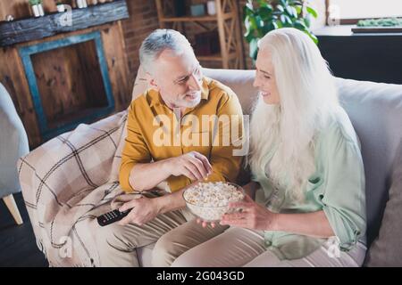 Foto von grauhaarigen glücklichen Menschen sitzen Sofa essen Pop Maisuhr tv Lächeln gute Laune drinnen im Haus Stockfoto