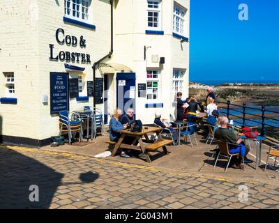 Menschen, die außerhalb des auf die Bestellung ihres Mittagessens warten Cod and Lobster Pub am Hafen von Staithes North Yorkshire im Herbst Stockfoto