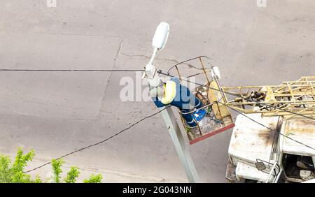 Ein Arbeiter in Schutzkleidung ersetzt die Glühbirnen in der Laterne. Ein Elektriker repariert eine Straßenlampe, ein Elektriker steigt auf einen Berg. Stockfoto