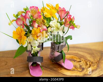 Geschenk für Behinderte, Sozialschutz, besondere Bedürfnisse, Blumensträuße in orthopädischen Orthesen platziert. Auf weißem Hintergrund. Stockfoto