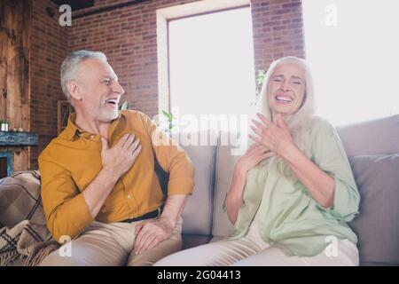 Porträt eines attraktiven, fröhlichen, grauhaarigen Paares, das auf dem Sofa sitzt und lacht Reden Spaß zu Hause Backstein Loft Innenhauswohnung Innen Stockfoto