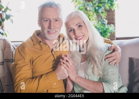 Foto von charmanten fröhlichen alten Menschen Umarmung halten Hände Familie Smile Sit Sofa drinnen im Haus Wohnung Stockfoto