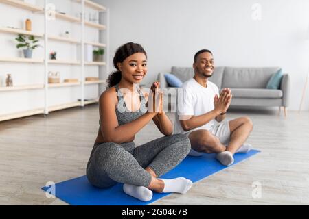 Home Yoga Üben während des Covid. Schwarzes Paar meditiert oder macht Atemübungen, sitzt zu Hause in Lotuspose Stockfoto