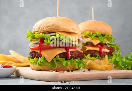 Zwei große, leckere Burger und Pommes auf grauem Hintergrund. Seitenansicht, Nahaufnahme. Stockfoto