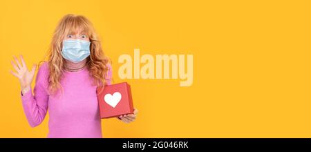 Erwachsene oder ältere Frau mit Gesichtsmaske isoliert auf dem Hintergrund Mit Geschenkbox mit Herz Stockfoto