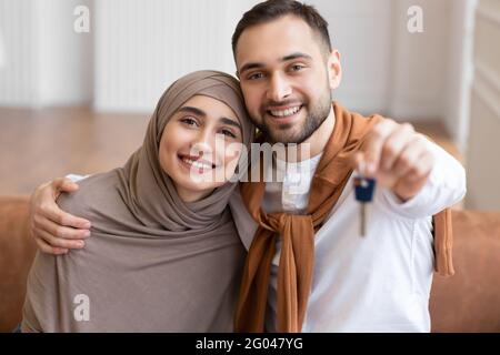 Glückliche Muslimische Ehegatten Zeigen Den Schlüssel Des Neuen Hauses Und Umarmen Sich Zu Hause Stockfoto