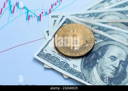 Goldbitcoin Kryptowährung Münze liegt auf hundert Dollar-Scheine Und Diagramme von Änderungen der Kryptowährungsrate Stockfoto
