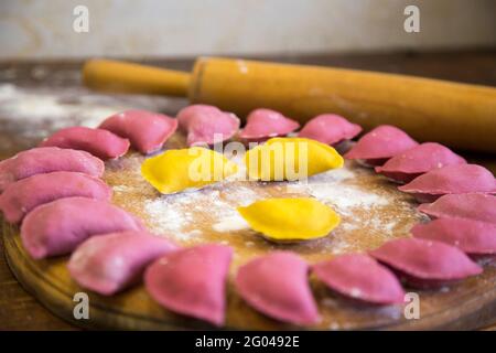 Gelb-rosa Knödel, für das Kochen ausgelegt, auf dem hölzernen Regen, slawische Nahrung. Ukrainisches Nationalgericht. Traditionelles Gericht der Prozess der Herstellung von Knödeln Stockfoto