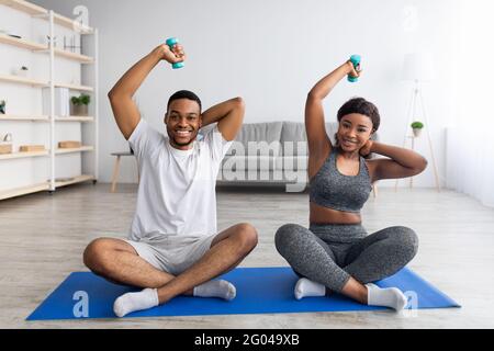 Fröhliches schwarzes Paar trainiert zu Hause mit Hanteln und macht häusliche Fitness während des covid Lockdown Stockfoto