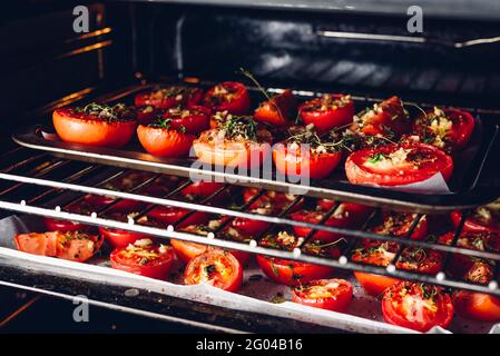 Halbierte Tomaten mit Kräutern und Knoblauch auf Backblech vorbereiten Im Ofen zum Konservieren Stockfoto