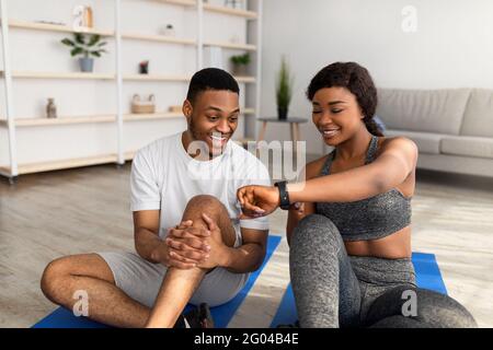 Sportliche schwarze Dame zeigt Daten auf Smartwatch oder Fitness Tracker An ihren Freund nach dem Training zu Hause Stockfoto