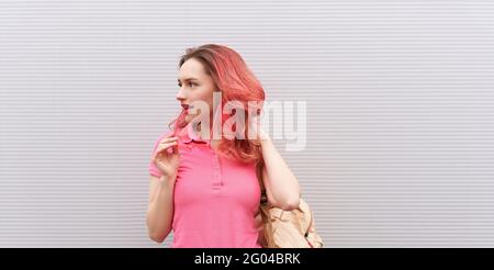 Schöne Frau mit rosa gefärbten Haaren und Neon-Sonnenbrille über der grauen Wand stehen. Fliegende Frisur Stockfoto