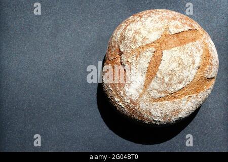Rundes Sauerteigbrot im Sonnenlicht auf einer dunklen metallischen Oberfläche. Platz für Text kopieren. Stockfoto