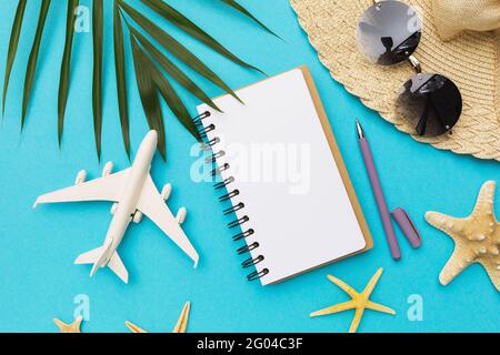 Leeres Notizbuch, Kugelschreiber, Spielzeugflugzeug und Sonnenbrille auf blauem Hintergrund. Stockfoto