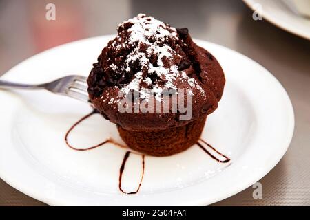 Ein Stück Chocolate Brownie mit Schokoladensauce und Puderzucker auf einem weißen Teller in einem Café. Junk-Food-Konzept. Hausgemachte Schokolade Brownies gekrönt Stockfoto