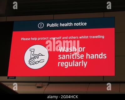 „regelmäßig Hände waschen oder desinfizieren“; roter Hinweis zur öffentlichen Gesundheit in der Abflughalle am Flughafen Luton, Mai 2021 Stockfoto