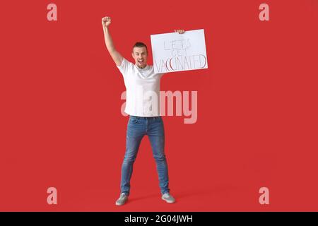 Glücklicher junger Mann mit Plakat mit Text LET'S IMPFEN LASSEN Auf farbigem Hintergrund Stockfoto