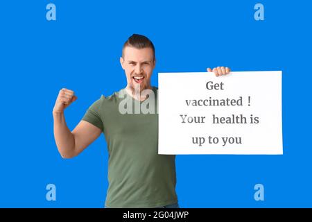Glücklicher junger Mann mit Plakat und Text IMPFEN LASSEN. IHRE GESUNDHEIT LIEGT BEI IHNEN auf farbigem Hintergrund Stockfoto