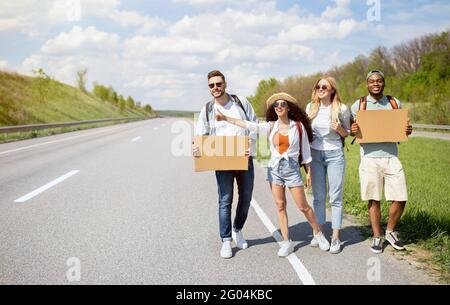 Gruppe multiethnischer Freunde mit leeren Schildern, die auf der Straße herumhiksten, eine Fahrt fangen, mit einem Autostop fahren, Platz kopieren Stockfoto