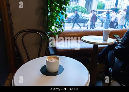 Saint-Petersburg, Russland - 25. Mai 2021: Starbucks Kaffeetasse auf einem Kaffeetisch und laute Straße hinter dem Fenster Stockfoto