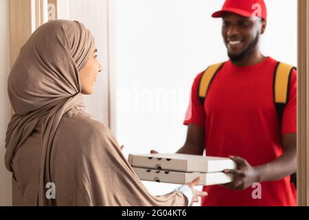 Schwarzer Lieferer hält und gibt Pizzaboxen Stockfoto
