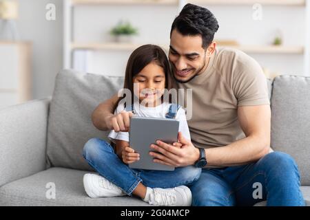 Lächelnder Vater und Tochter sitzen auf der Couch, mit digitalem Tablet Stockfoto