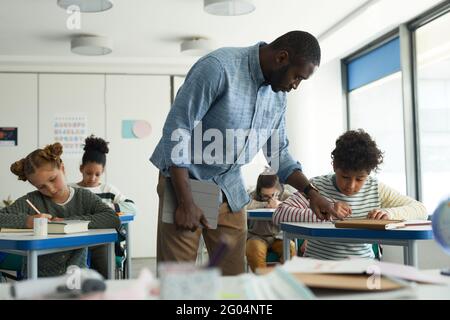 Porträt eines afroamerikanischen Lehrers, der Kindern im Klassenzimmer hilft Stockfoto