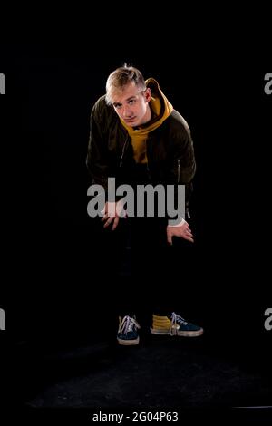 Trendy jungen Mann in sportlicher Jacke posiert in modernen Studio gegen schwarze Wand gekleidet Stockfoto