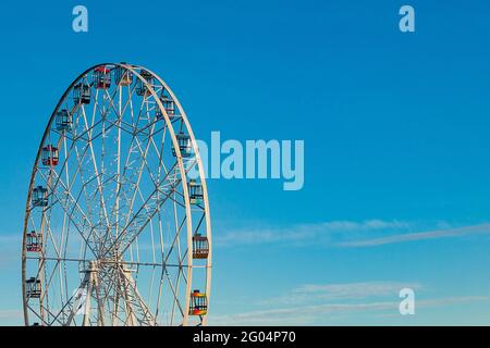 Hohes Riesenrad mit mehrfarbigen Kabinen auf blauem Himmel. Stockfoto