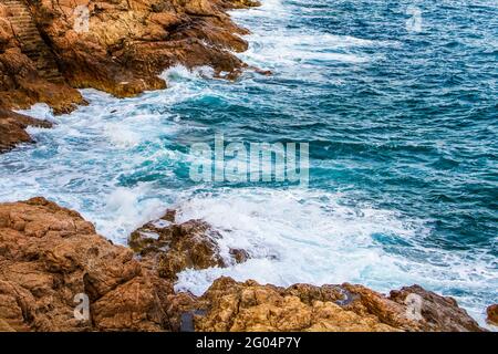 Tidalbohrung. Schaumig blaue Wellen krachen auf Küstenklippen. Stockfoto