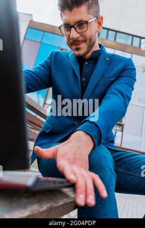 Arbeiten mit Vergnügen. Seitenansicht eines lächelnden jungen Mannes, der im Freien auf einem Laptop arbeitet Stockfoto