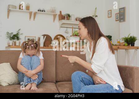 Alleinerziehende Mutter und kleines Kind sitzen zu Hause auf der Couch, Eltern schimpft Vorschultochter. Das Mädchen begrub ihr Gesicht auf den Knien und war kryoinend Stockfoto